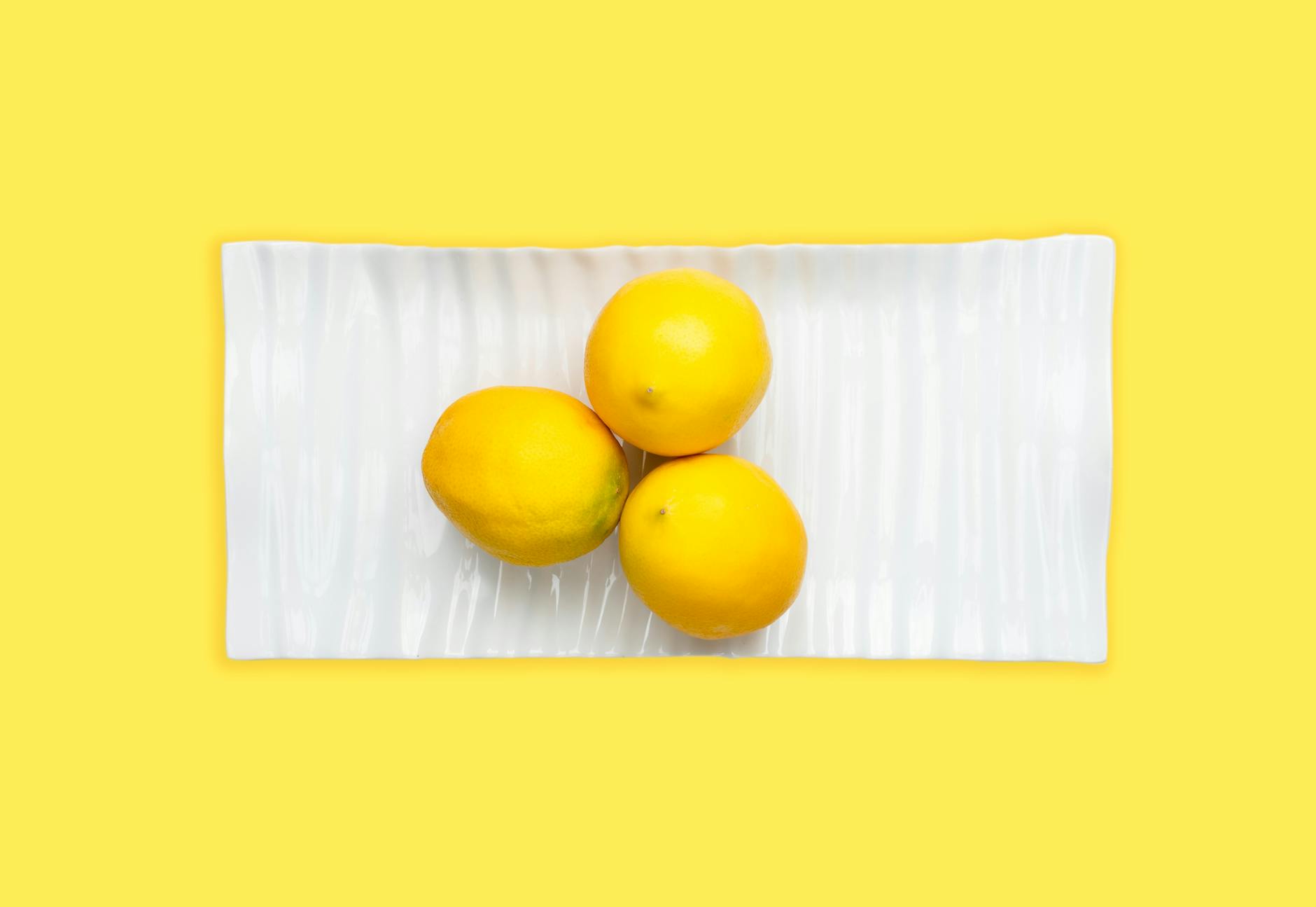 Limones frescos en un plato blanco sobre un fondo amarillo vibrante, simbolizando sensación y estimulación renovada