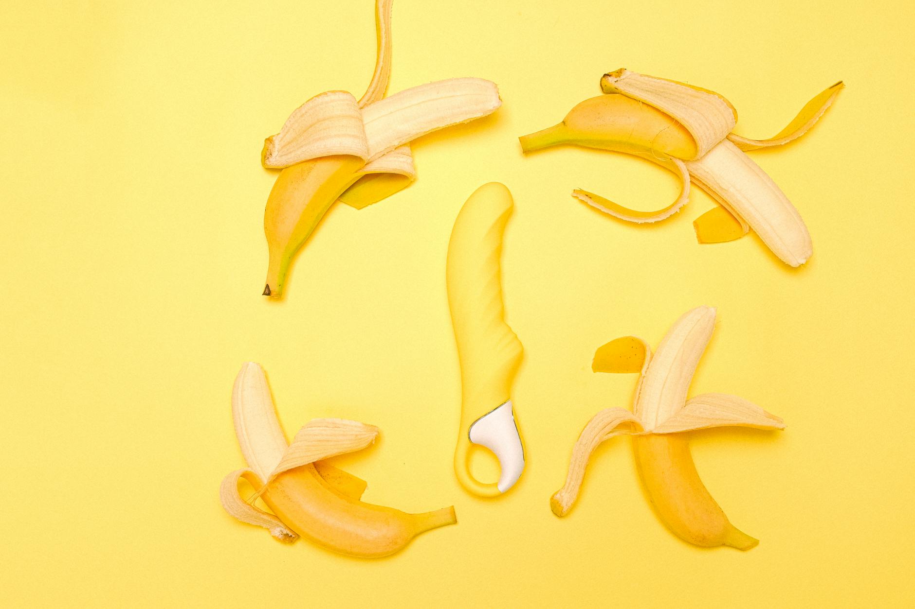 Yellow lemon-shaped vibrator surrounded by fresh peeled lemons on a bright yellow background
