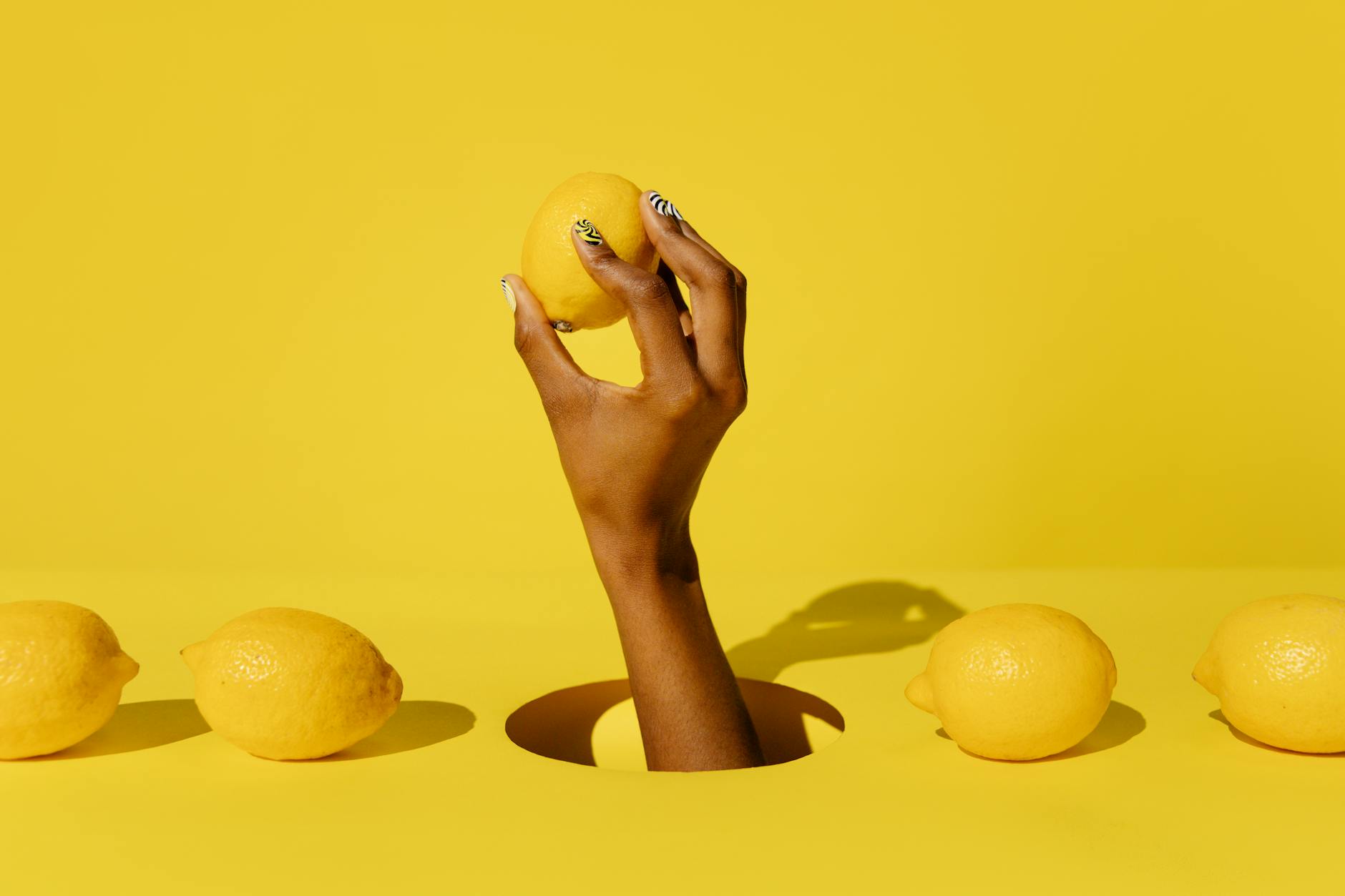 A hand holding a fresh lemon against a bright yellow background, symbolizing the Lem vibrator