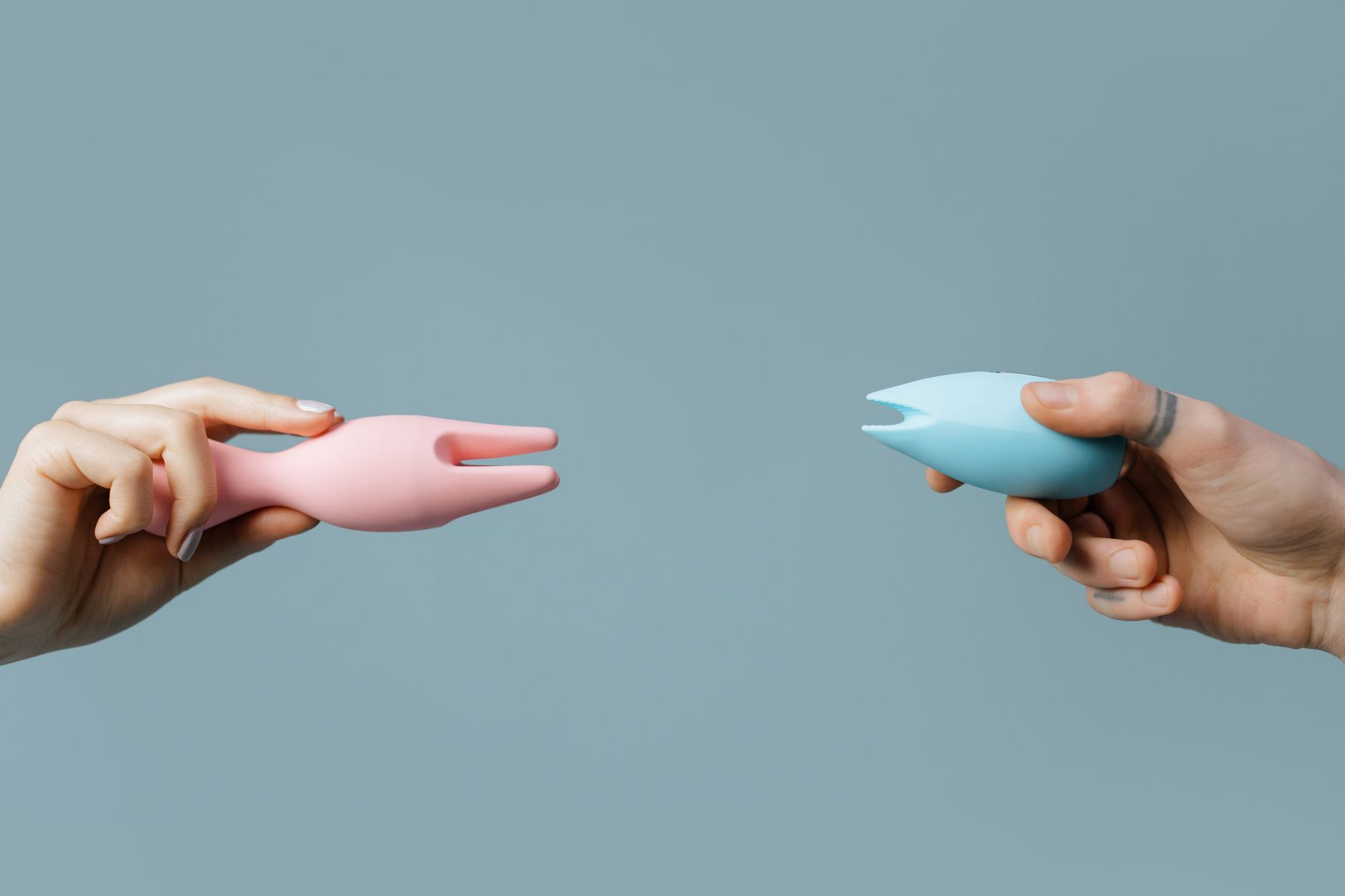Person holding blue and pink clitoral vibrators in a thoughtful pose