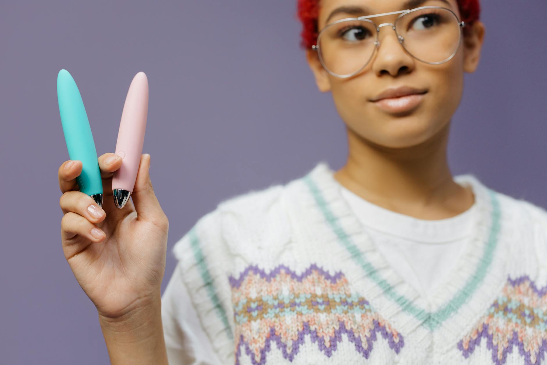 Woman holding colorful vibrators against a purple background, exploring pleasure on her own terms.