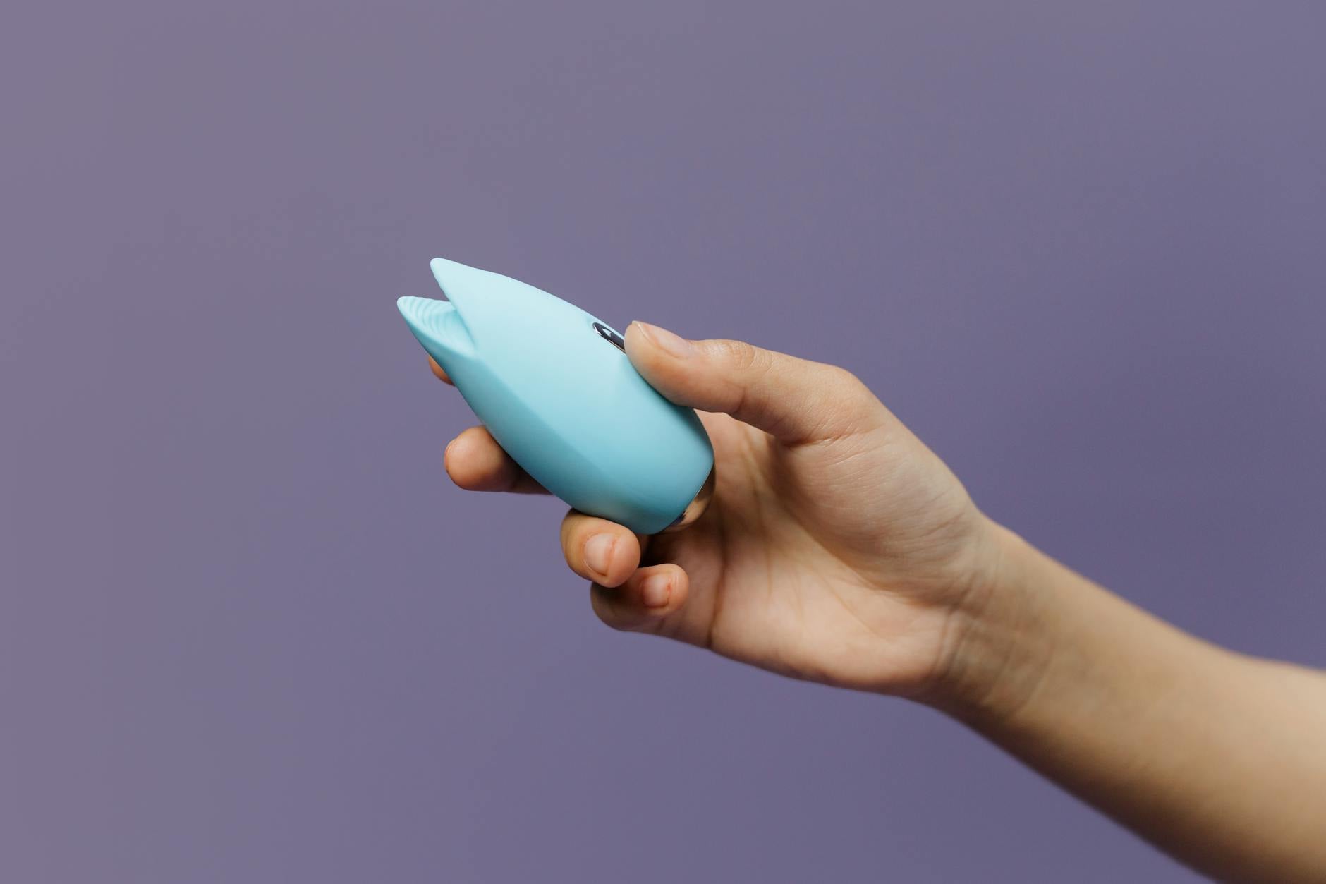 Manos sosteniendo un vibrador azul elegante contra un fondo púrpura pastel