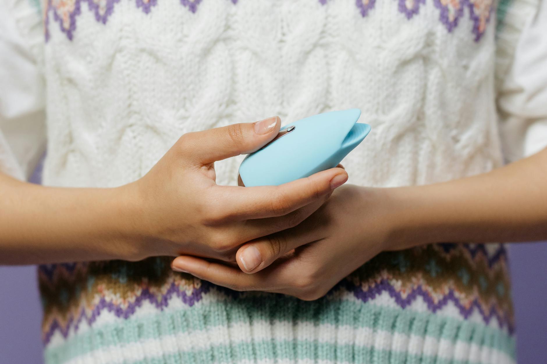 Close-up of hands holding a lemon vibrator against a knitted sweater, intimate and grounded.